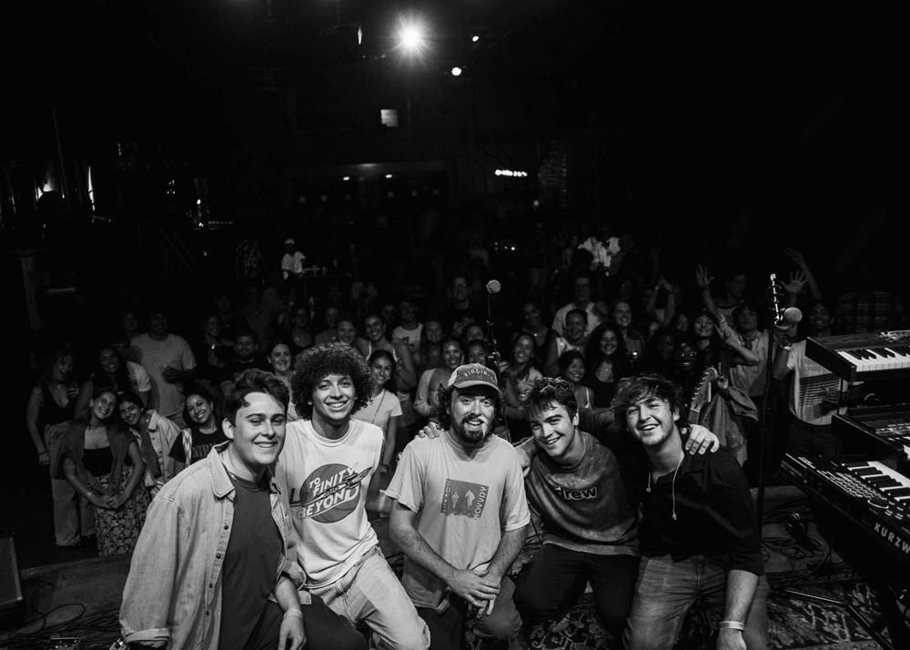 Band together posing and smiling with crowd smiling and cheering in background after their show in Nola
